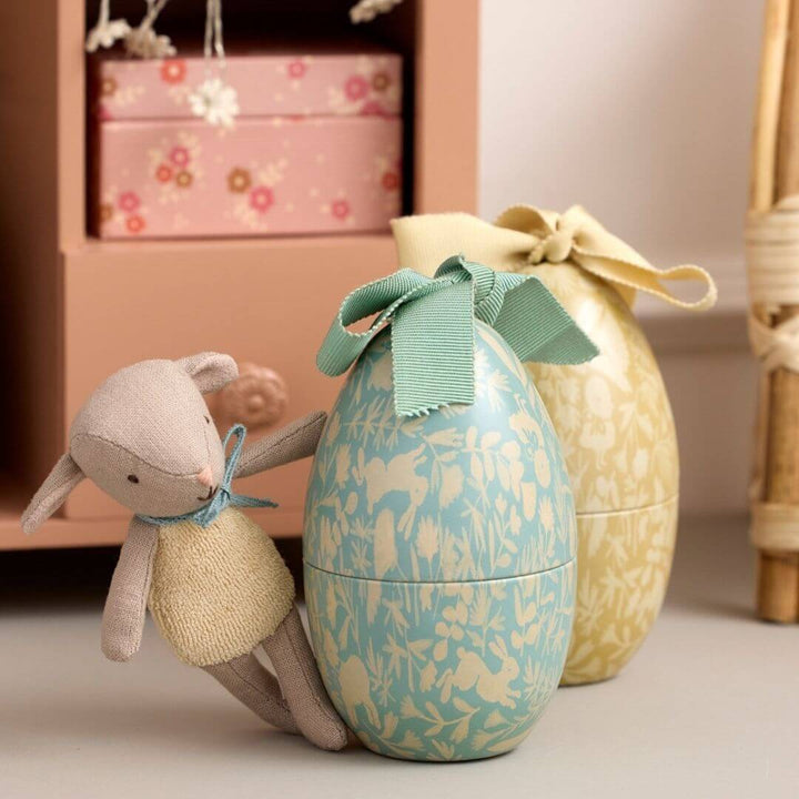Maileg stuffed lamb leaning against mint floral metal Easter egg with ribbon bow, yellow egg in background