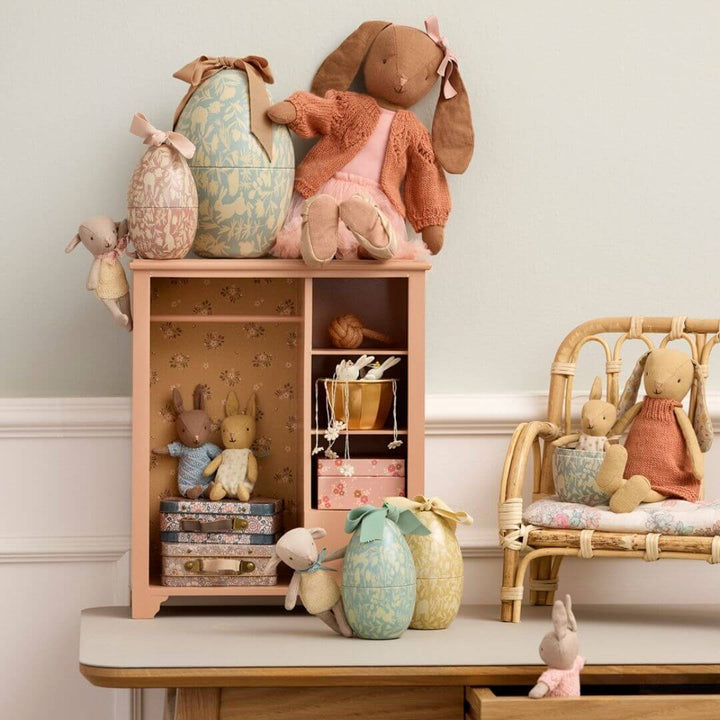 A nursery scene with Maileg bunnies and rabbits and the Maileg stuffed lamb leaning against mint floral metal Easter egg with ribbon bow, yellow egg in background