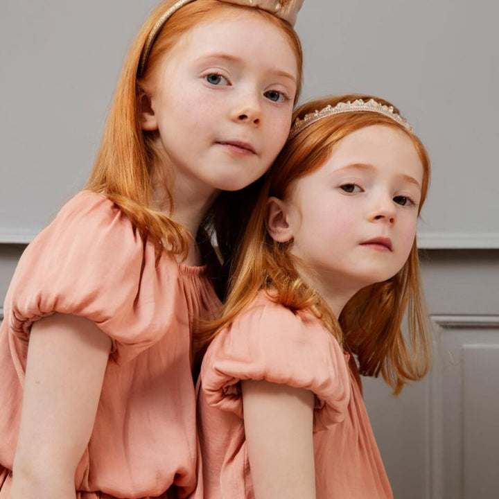 Two young girls in matching dresses with tiaras against a neutral background