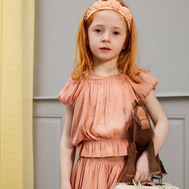 Young girl in a peach dress and headband standing against a neutral background