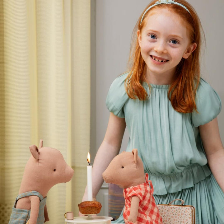 Young girl in a light green dress sitting with toy animals and a candle, smiling.