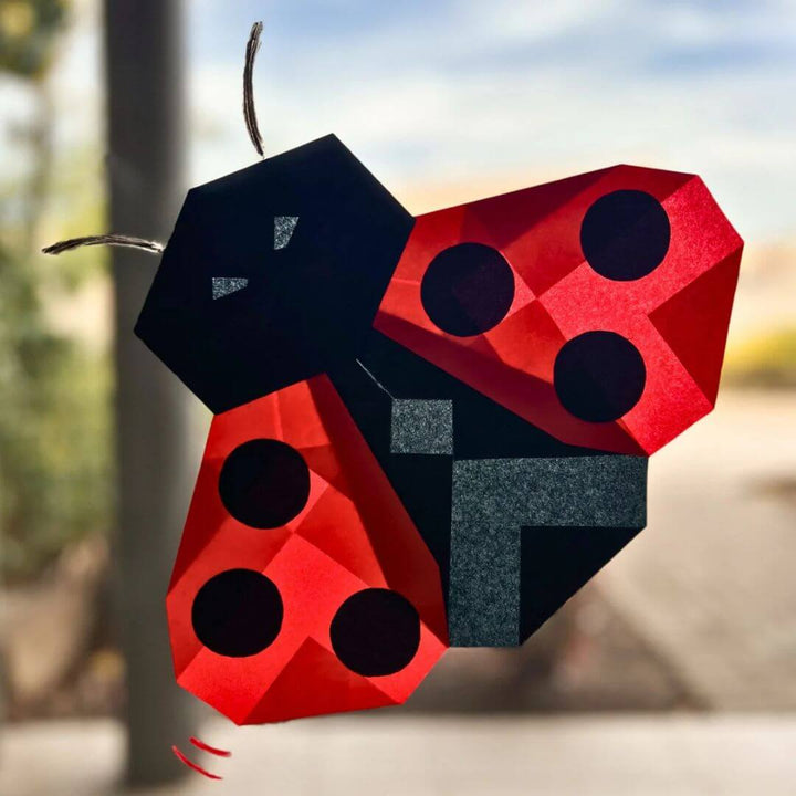 A folded Japanese silk paper red and black ladybug with a blurred outdoor background