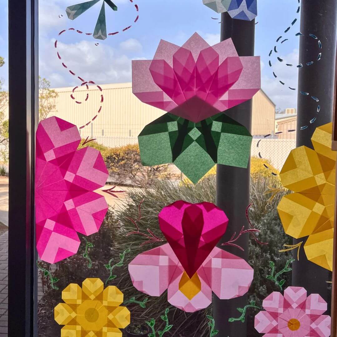 Decorative folded Japanese silk paper flowers on a glass door with a blurred outdoor background