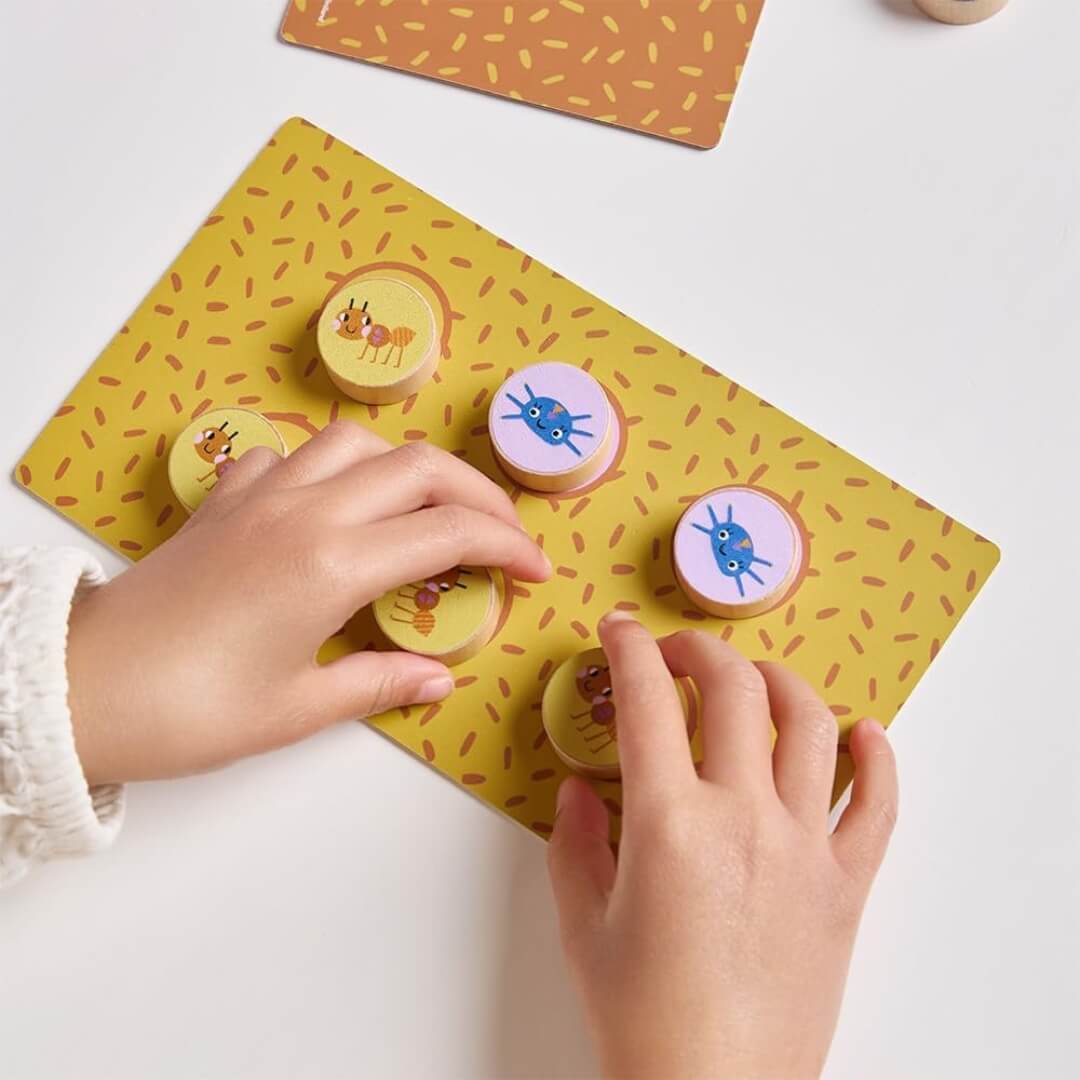 A close up of children's hands holding the wooden bug discs on a game board in Catch the Bug game from Miniland. 
