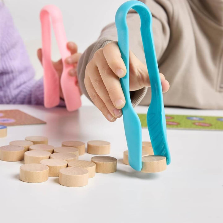 A close up of a child holding blue tweezers and picking up a wooden disc in the Catch the Bug game from Miniland. 
