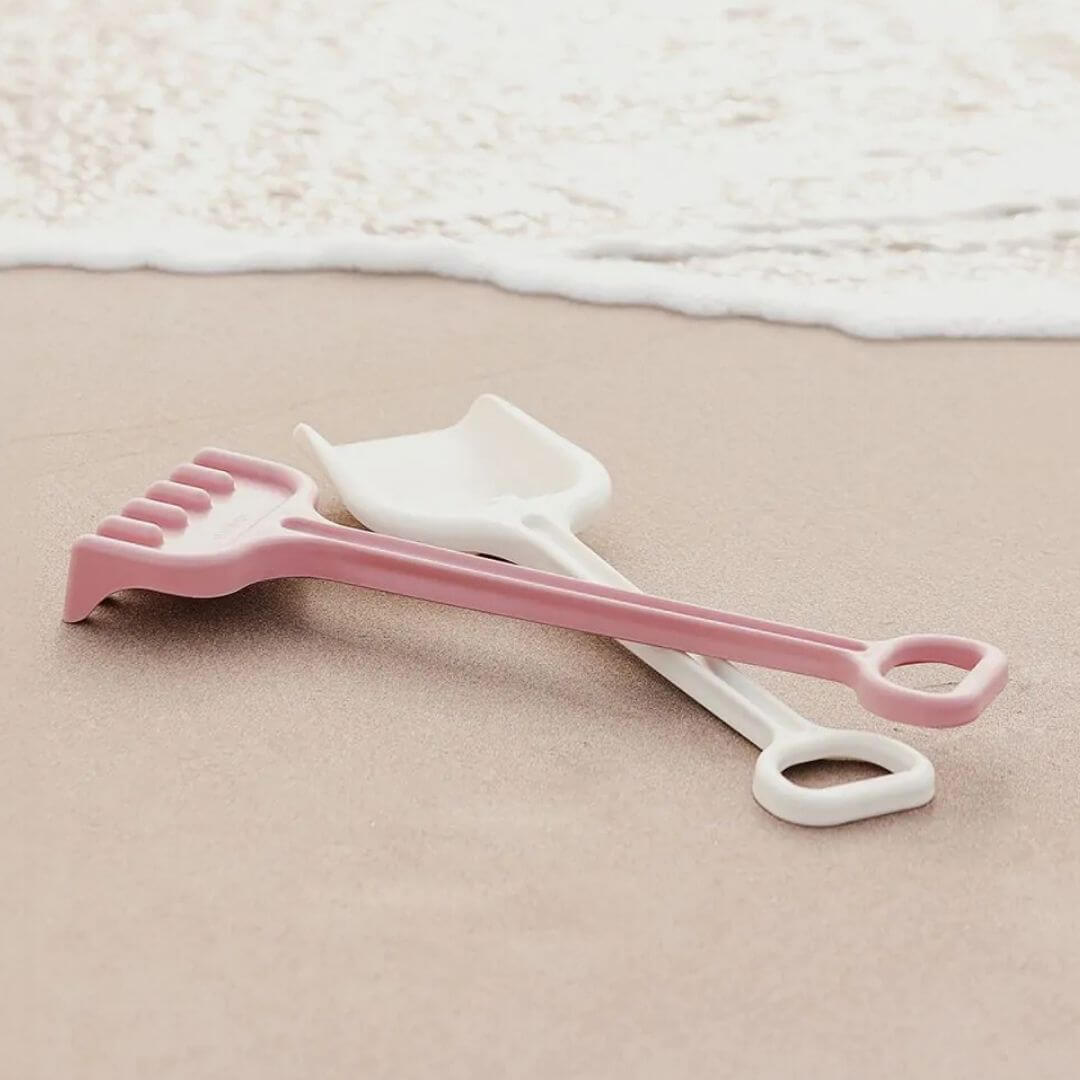 Miniland - ECO Rake & Spade Set placed on the sand with ocean in the background - Bella Luna Toys