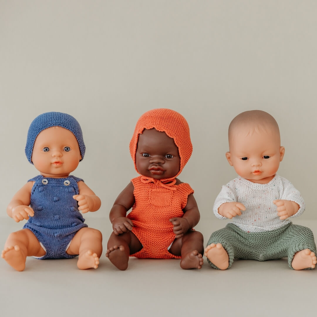 3 Miniland dolls in knit clothing sitting in a row.