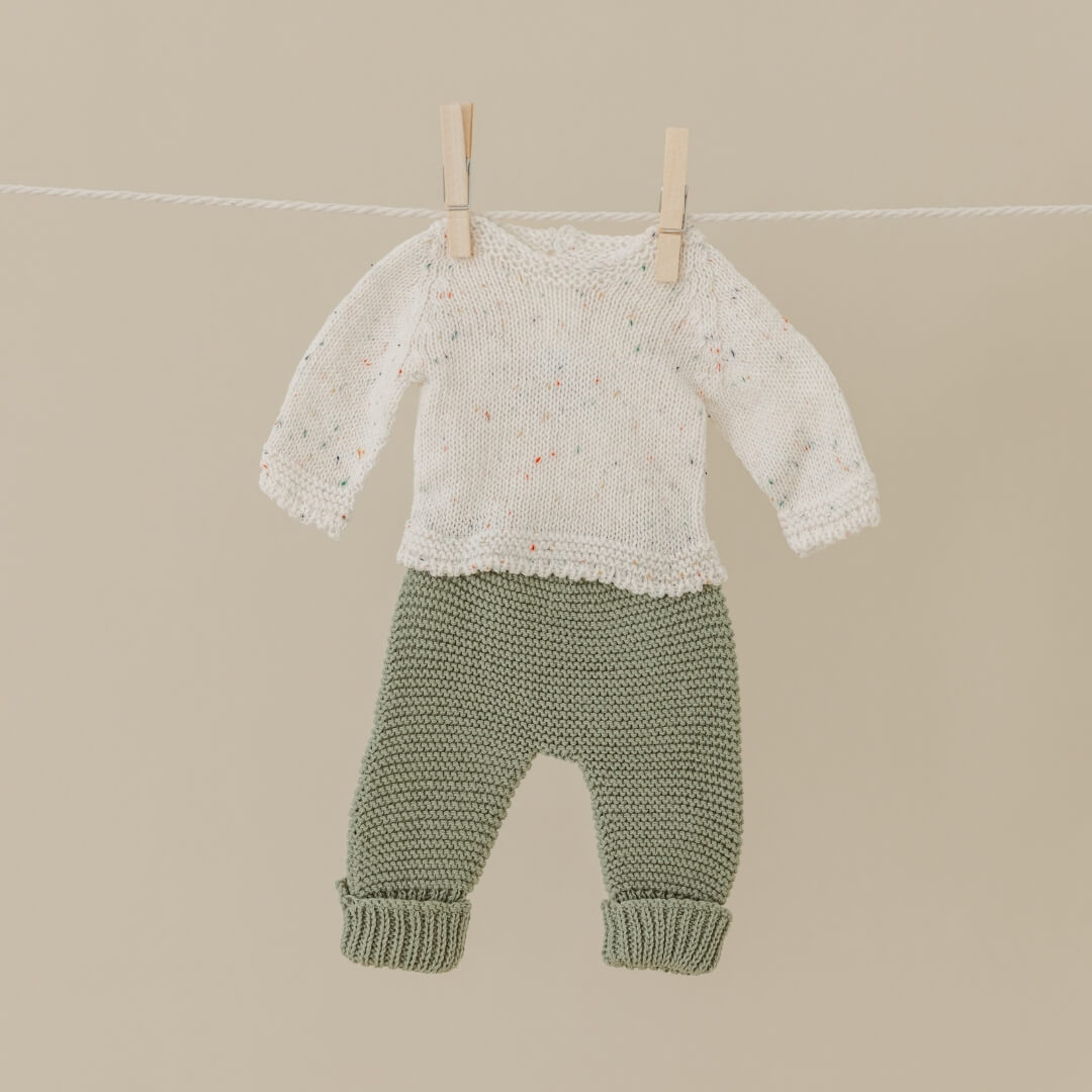 Baby sweater and pants hanging on a clothesline against a beige background
