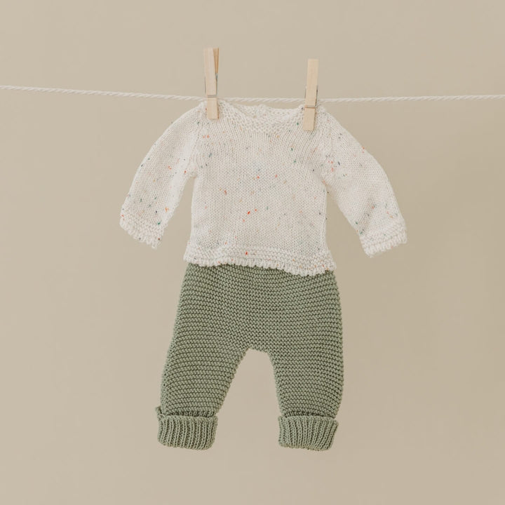 Baby sweater and pants hanging on a clothesline against a beige background