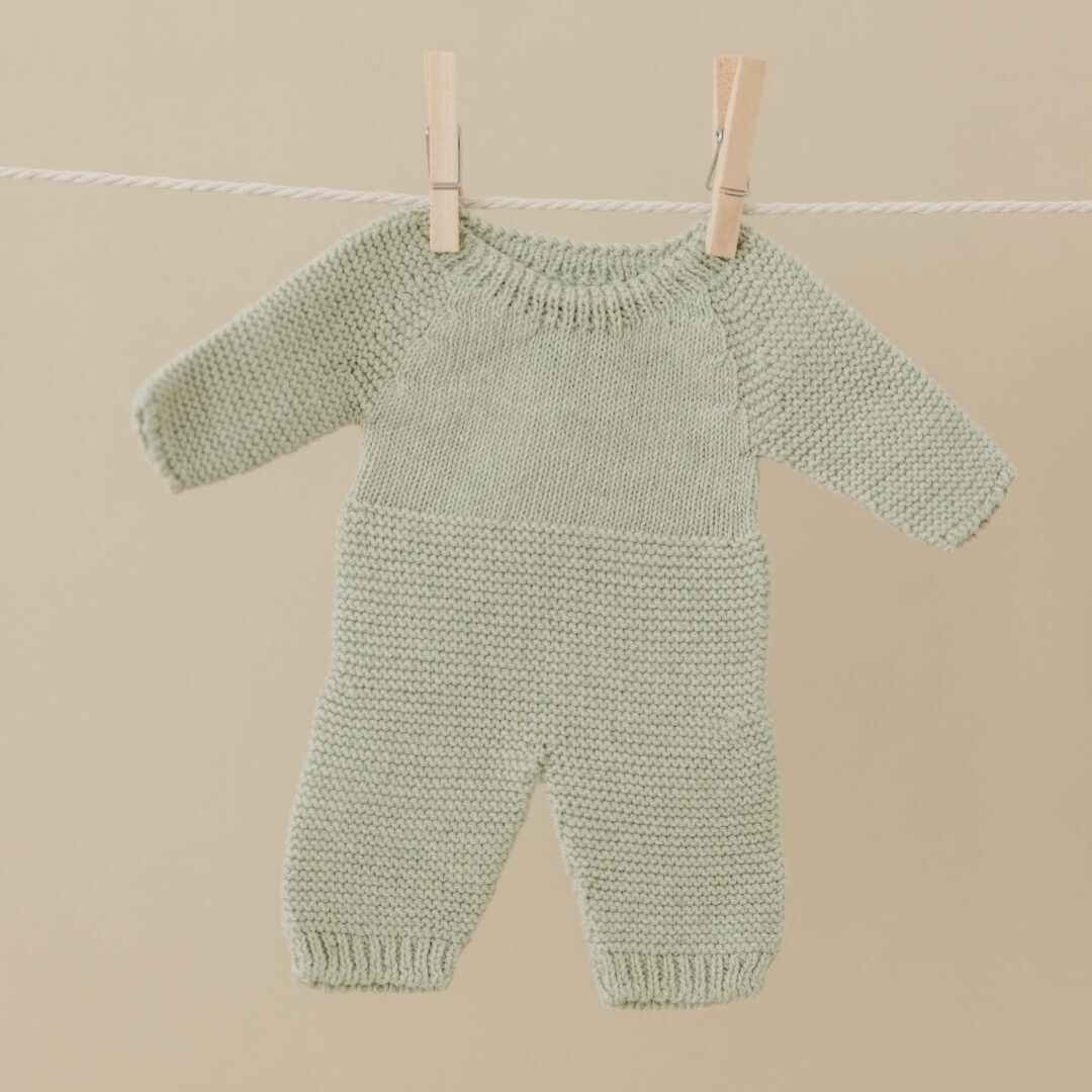Knitted Sage green pajamas for 12-inch Miniland Dolls, made from recycled materials with a handmade feel—eco-friendly and perfect for pretend play hanging on a line against a beige background