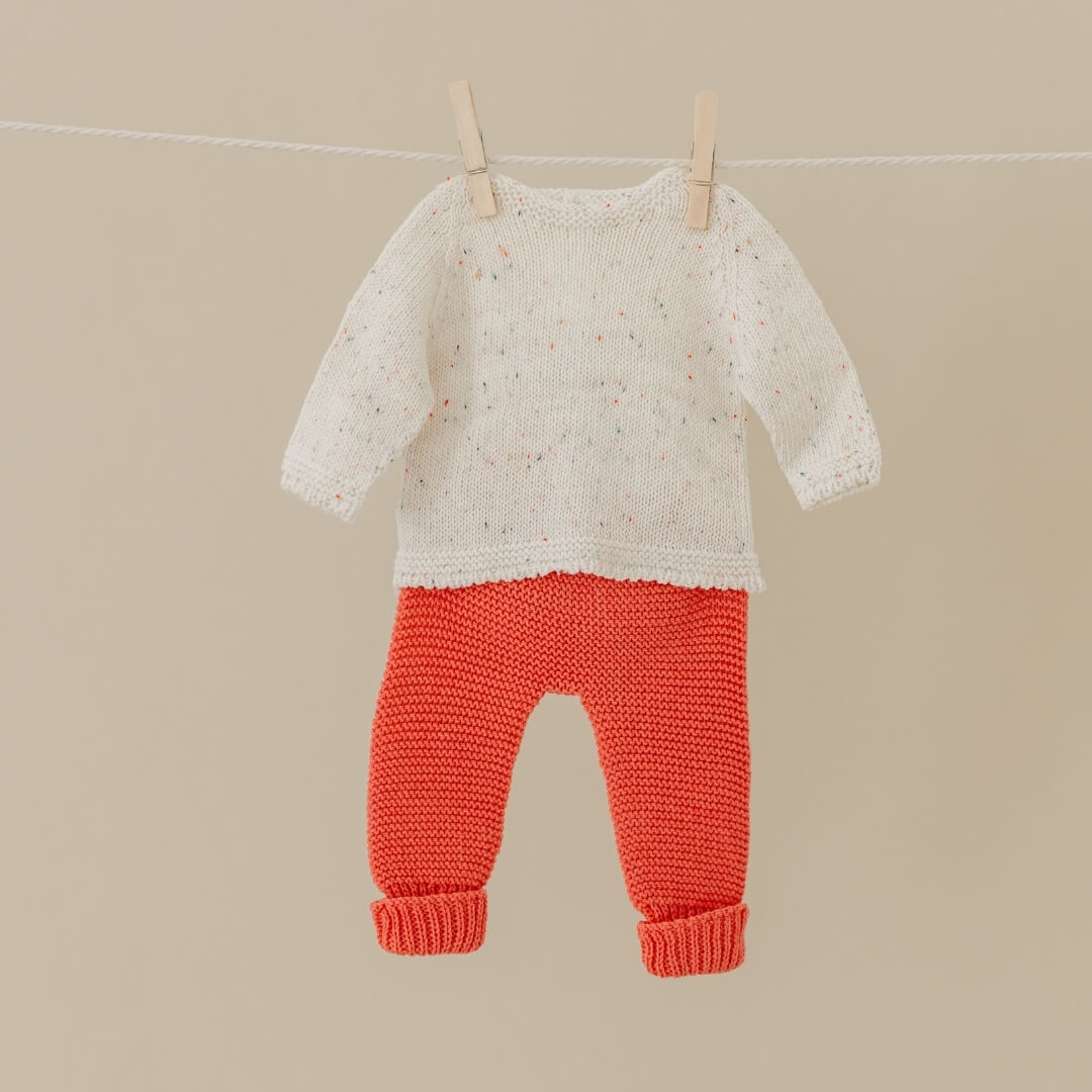 Knitted cream sweater and red pants set for 15-inch Miniland Dolls, made from recycled materials with a soft, handmade look—hanging on a clothesline against a beige background