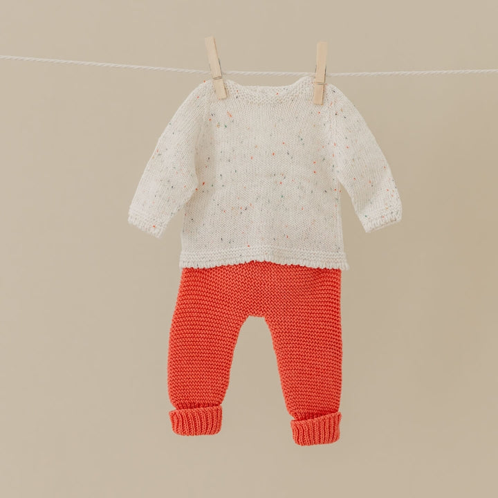 Knitted cream sweater and red pants set for 15-inch Miniland Dolls, made from recycled materials with a soft, handmade look—hanging on a clothesline against a beige background