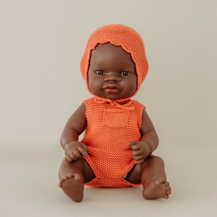 Baby doll wearing an orange knitted outfit on a beige background
