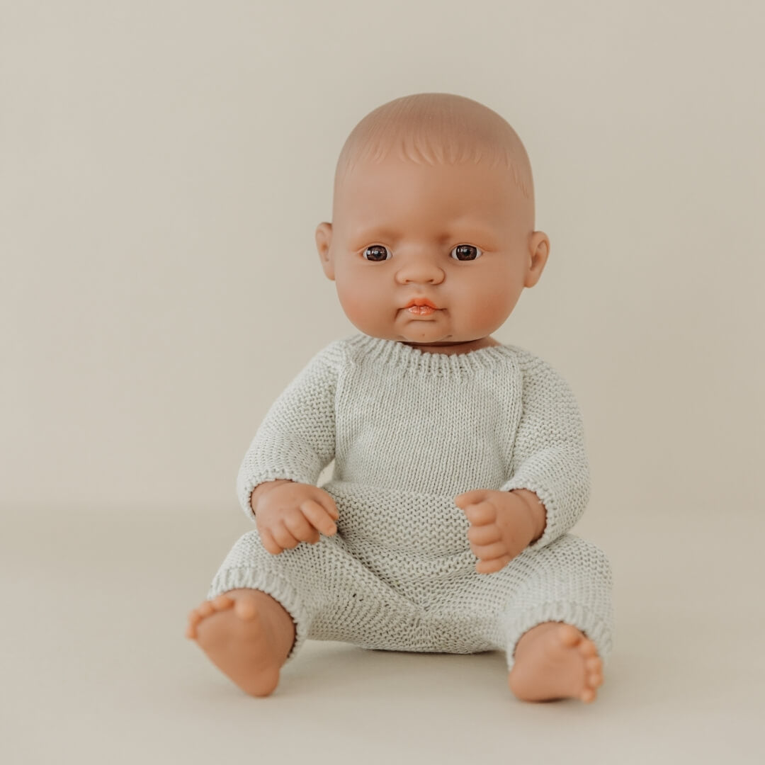 Miniland Realistic baby doll wearing pale sage green knitted pajamas for 12-inch Miniland Dolls, made from recycled materials with a handmade feel—eco-friendly and perfect for pretend play on a beige background