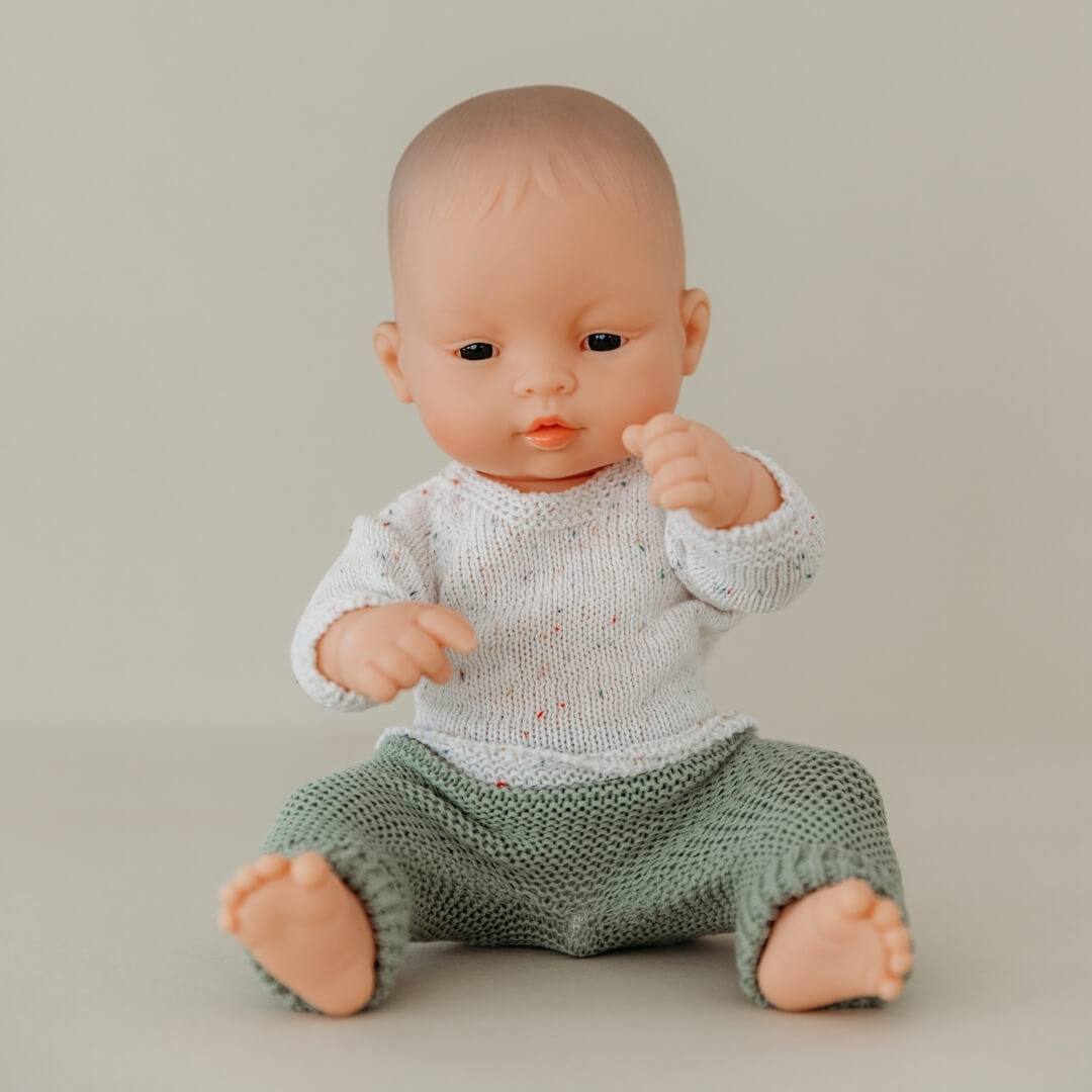 Baby doll wearing a knitted outfit on a plain background