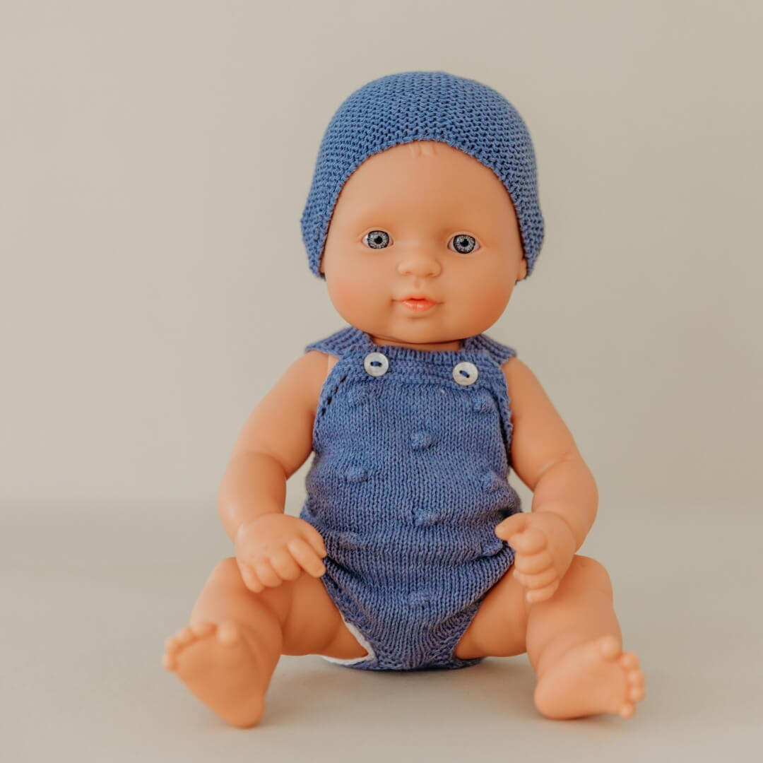 Baby doll wearing a blue knitted outfit and hat on a plain background