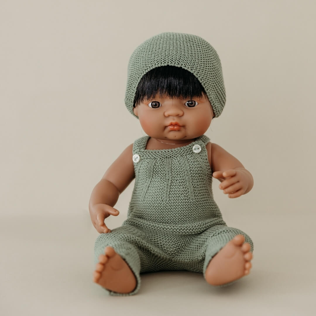 Doll wearing a green knitted outfit and hat on a beige background