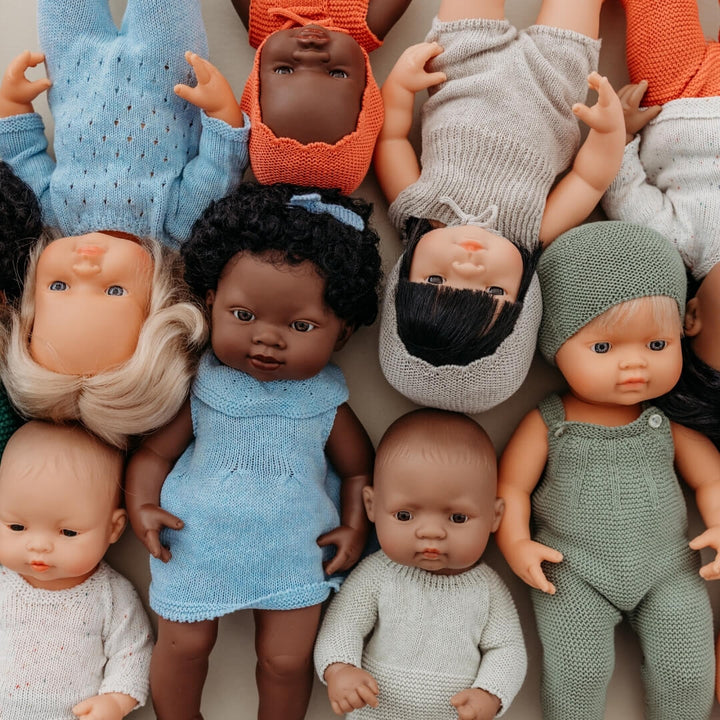Group of dolls with various outfits and skin tones on a neutral background