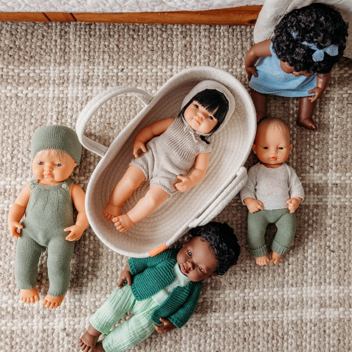 Five Miniland dolls in knit clothing laying on a brown and white rug.