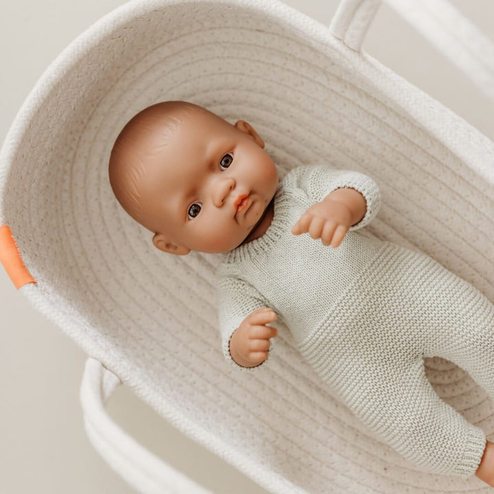 Minland Realist baby doll in pale sage green knitted pajamas for 12-inch Miniland Dolls, made from recycled materials with a handmade feel—eco-friendly and perfect for pretend play lying in a textured basket.
