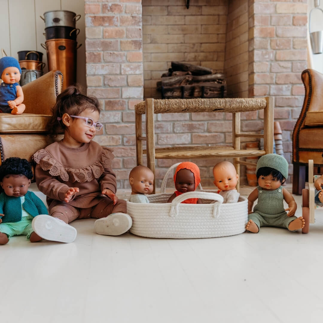A child sitting on the floor surrounded by Miniland dolls and the doll carrier basket.