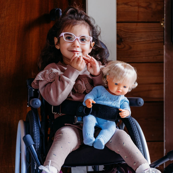 Child in a wheelchair holding a Miniland Realistic doll wearing the blue knit pajamas for 15-inch dolls, made from recycled materials with a handmade look—part of Miniland's eco-friendly doll clothing collection.