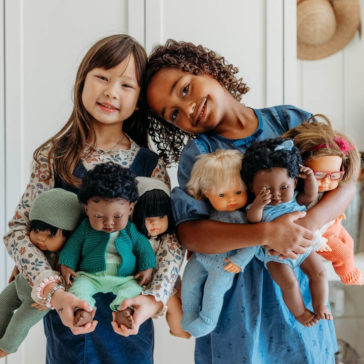 Two girls holding six Miniland dolls in their arms.