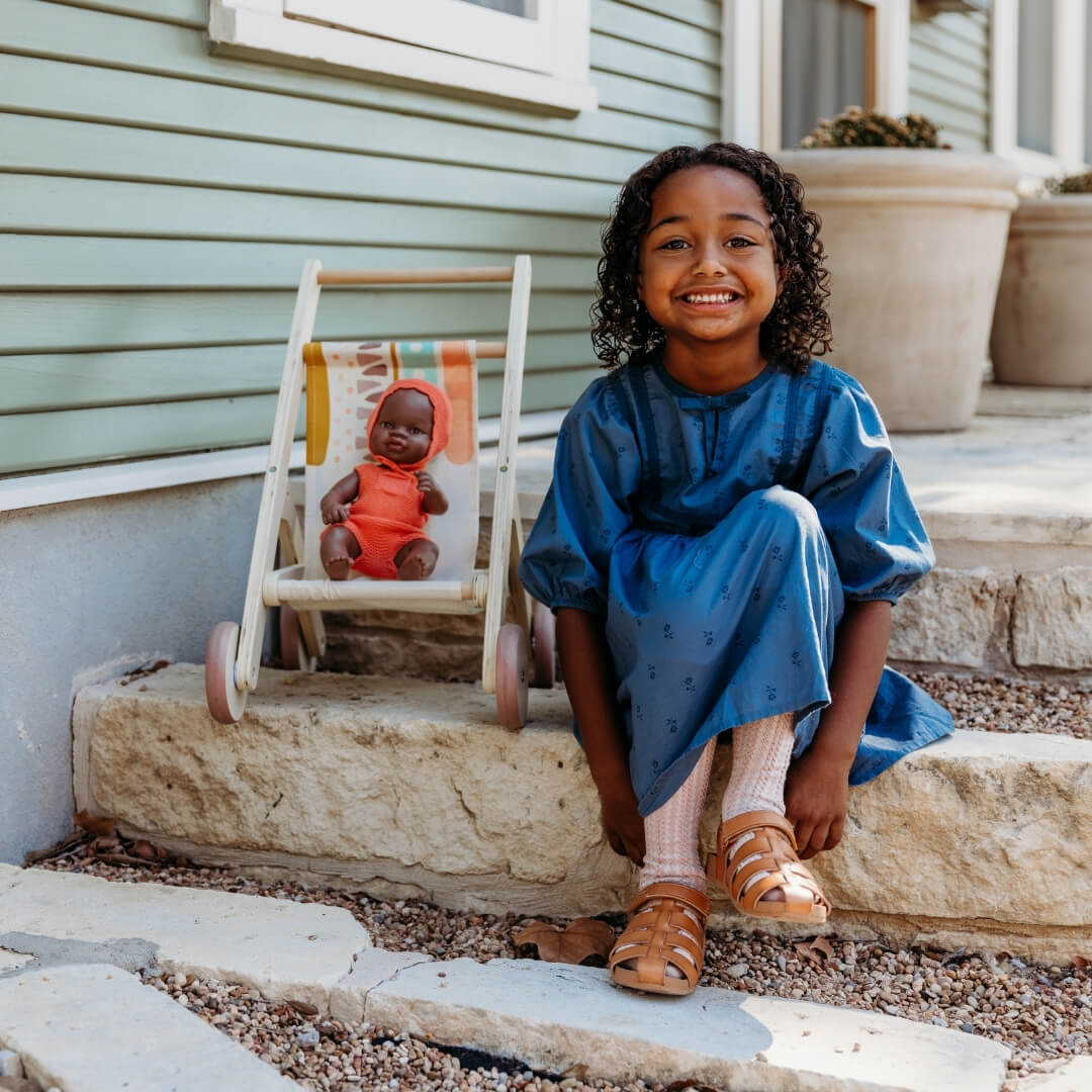 Child in a blue dress sitting on steps next to a toy with a doll, outside a house.