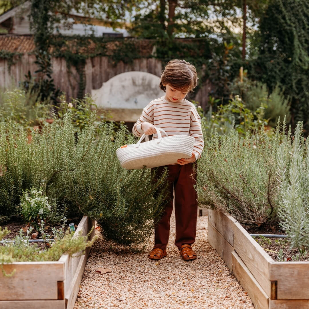 A child holding the Miniland doll carrier in a garden.