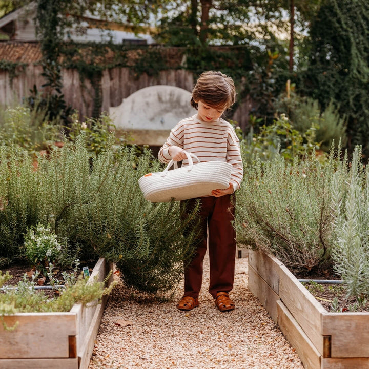 A child holding the Miniland doll carrier in a garden.