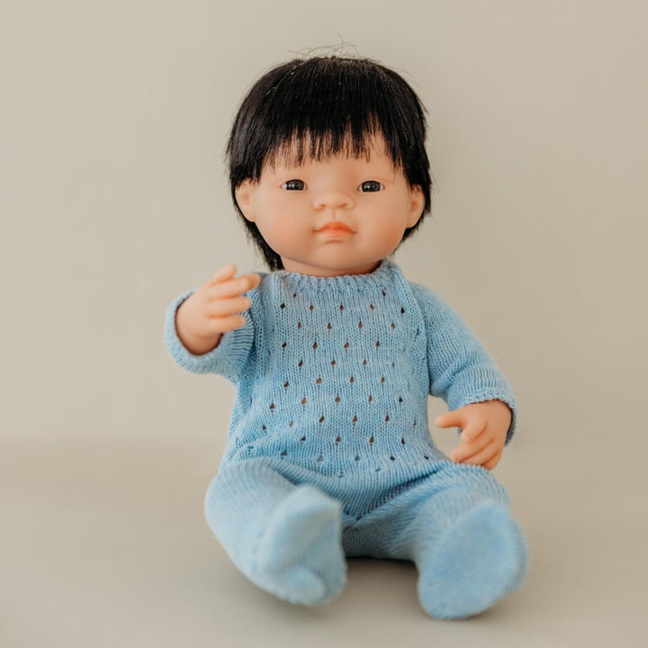 Miniland realistic boy doll wearing blue knit pajamas for 15-inch dolls, made from recycled materials with a handmade look—part of Miniland's eco-friendly doll clothing collection on a beige background