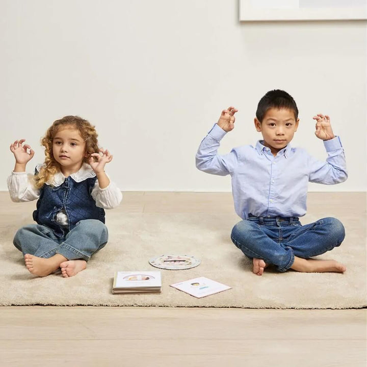 Two children sit cross-legged on a light-colored rug playing Miniland's Spin & Chill mindfulness and relaxation game. 