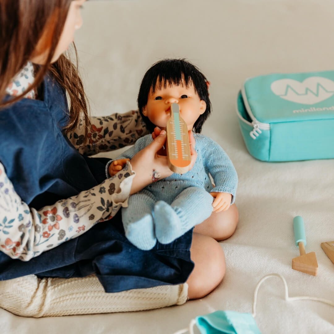 A child using the pretend play wooden doctor kit from Miniland to care for her Miniland doll.