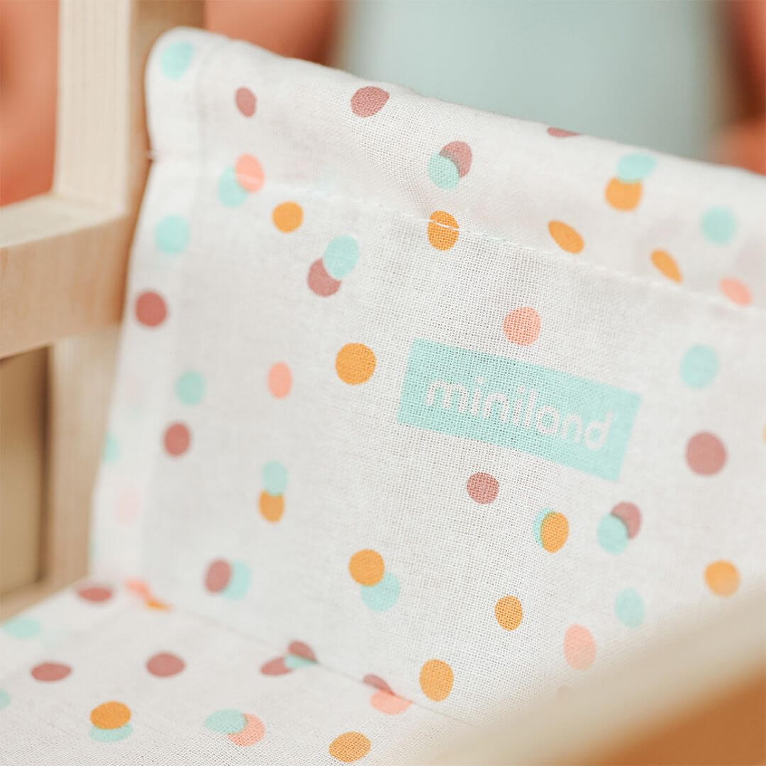 A close up of the polka dot fabric seat of the Miniland Wooden Doll Wheelchair designed to fit 14-inch dolls.