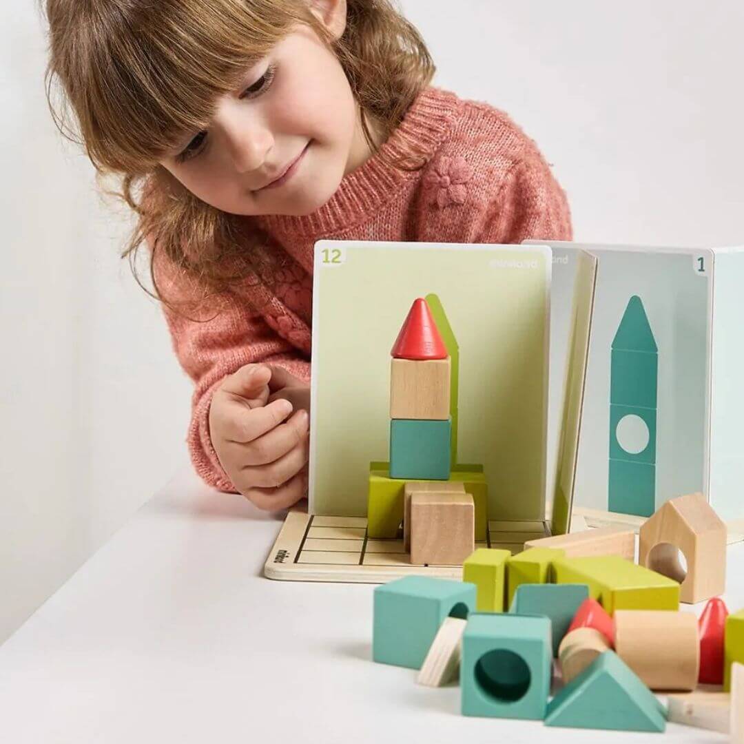 Miniland -  Child plays with Shape Makers learning game with 40 colorful wooden building pieces, 24 challenge cards, and 4 player boards in a playroom setting - Bella Luna Toys - Bella Luna Toys