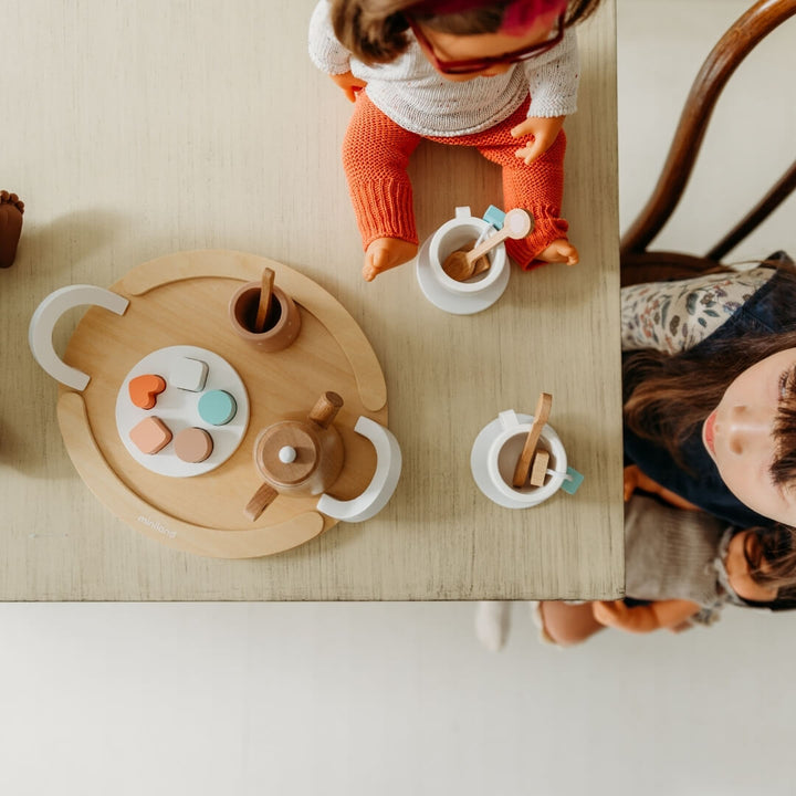 Children playing with a wooden tea set on a table.