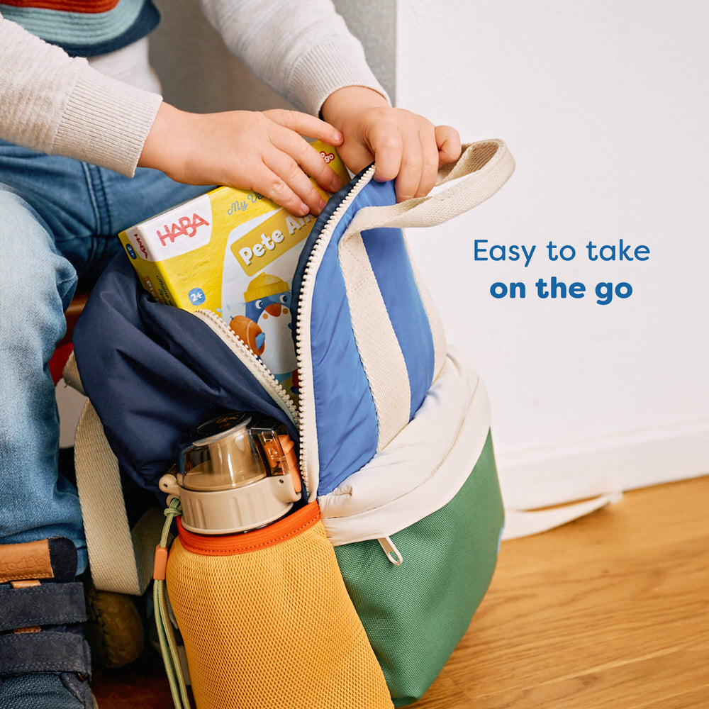 Colorful bag with a child's hands opening it, containing a HABA game and thermos.