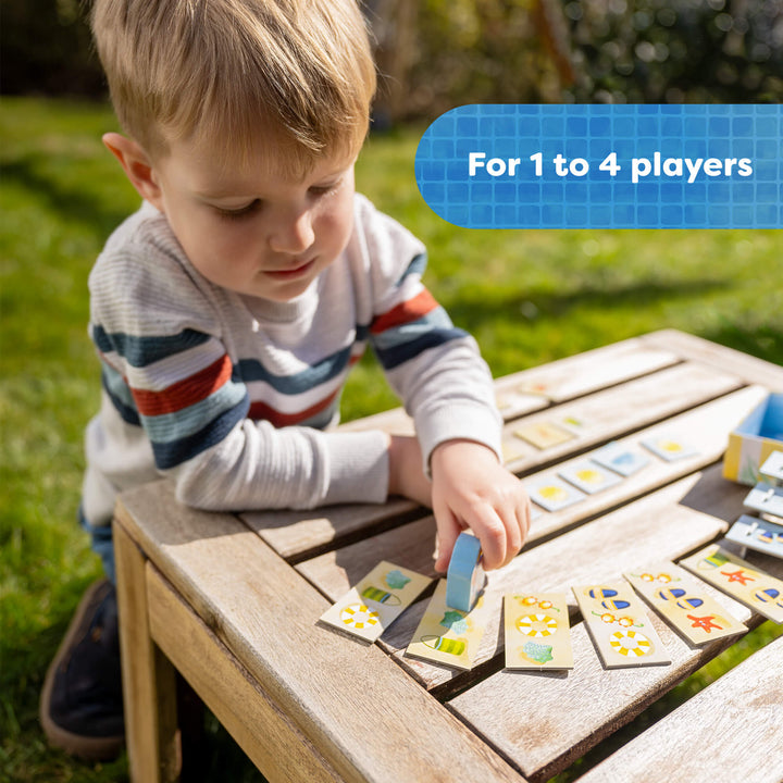 Child playing with a board game outdoors on a wooden table.