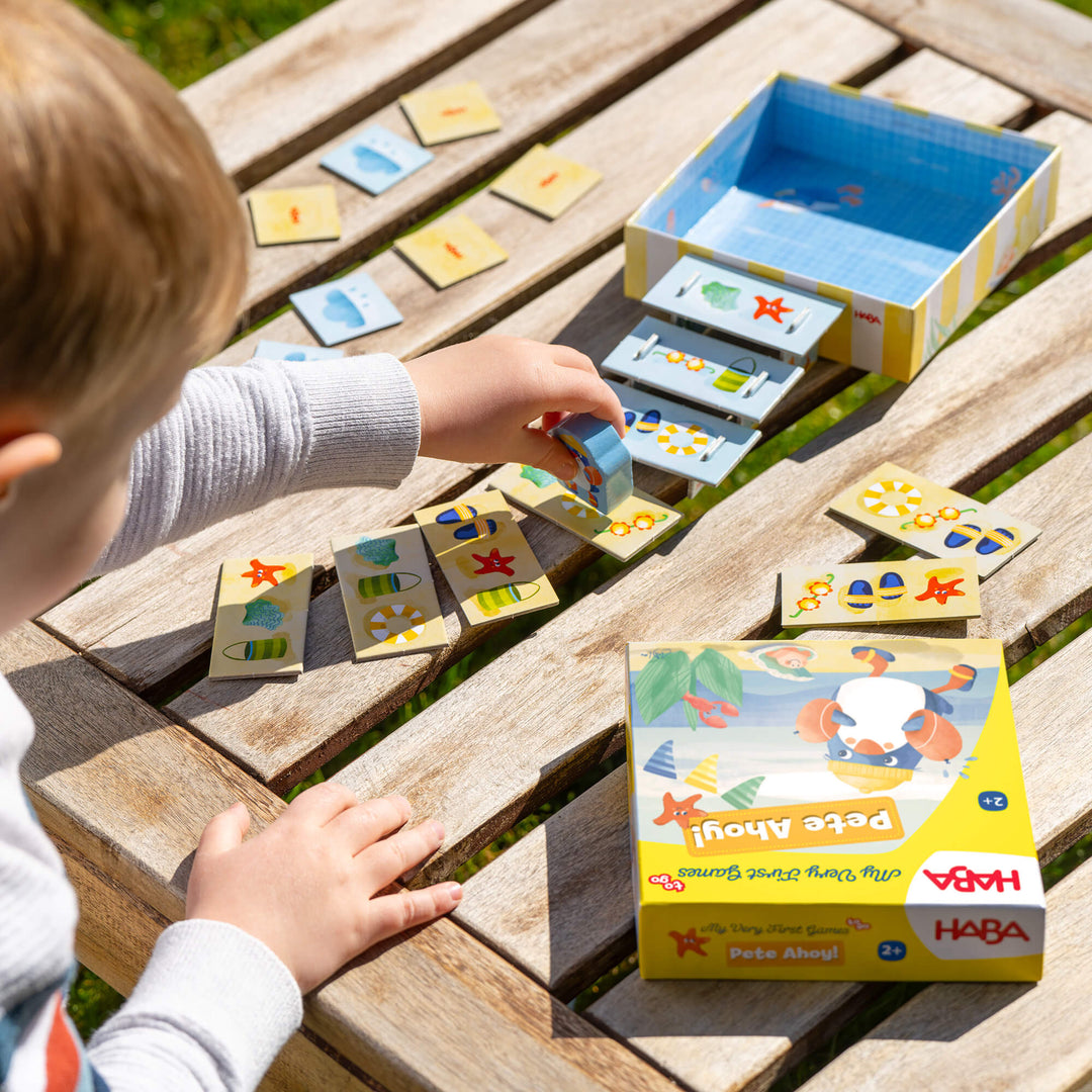 Child playing with a HABA Pete Ahoy game on a wooden table outdoors