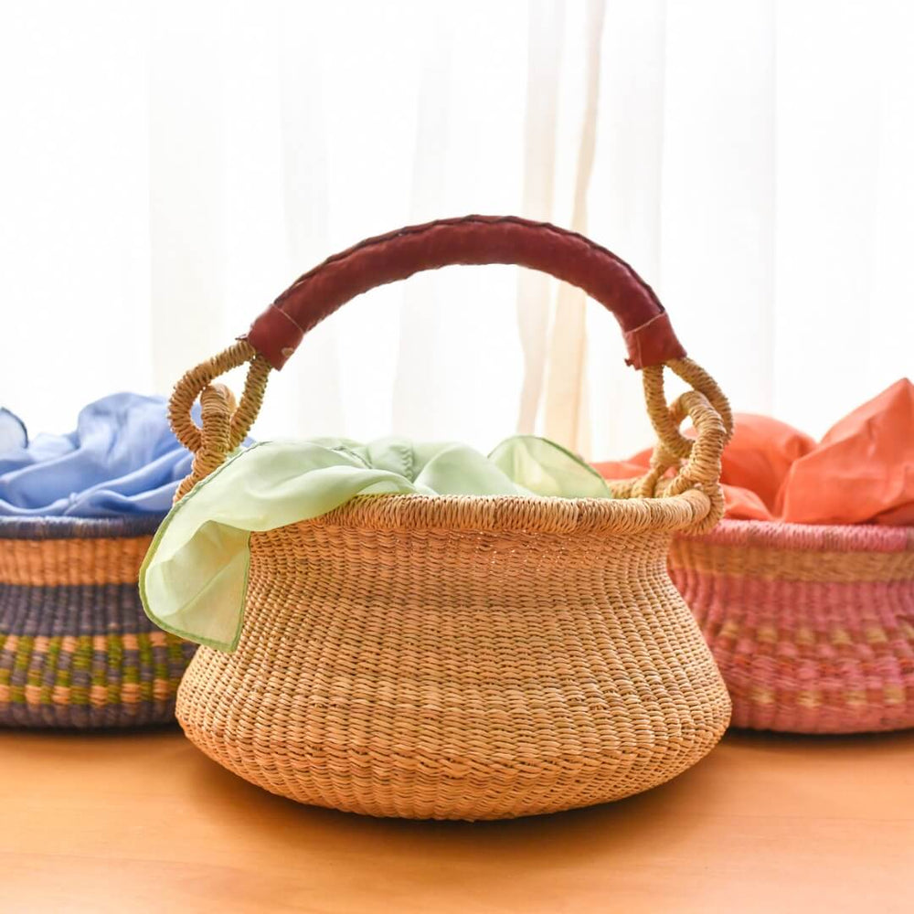 A natural swing bolga basket sitting in front of two colorful versions.