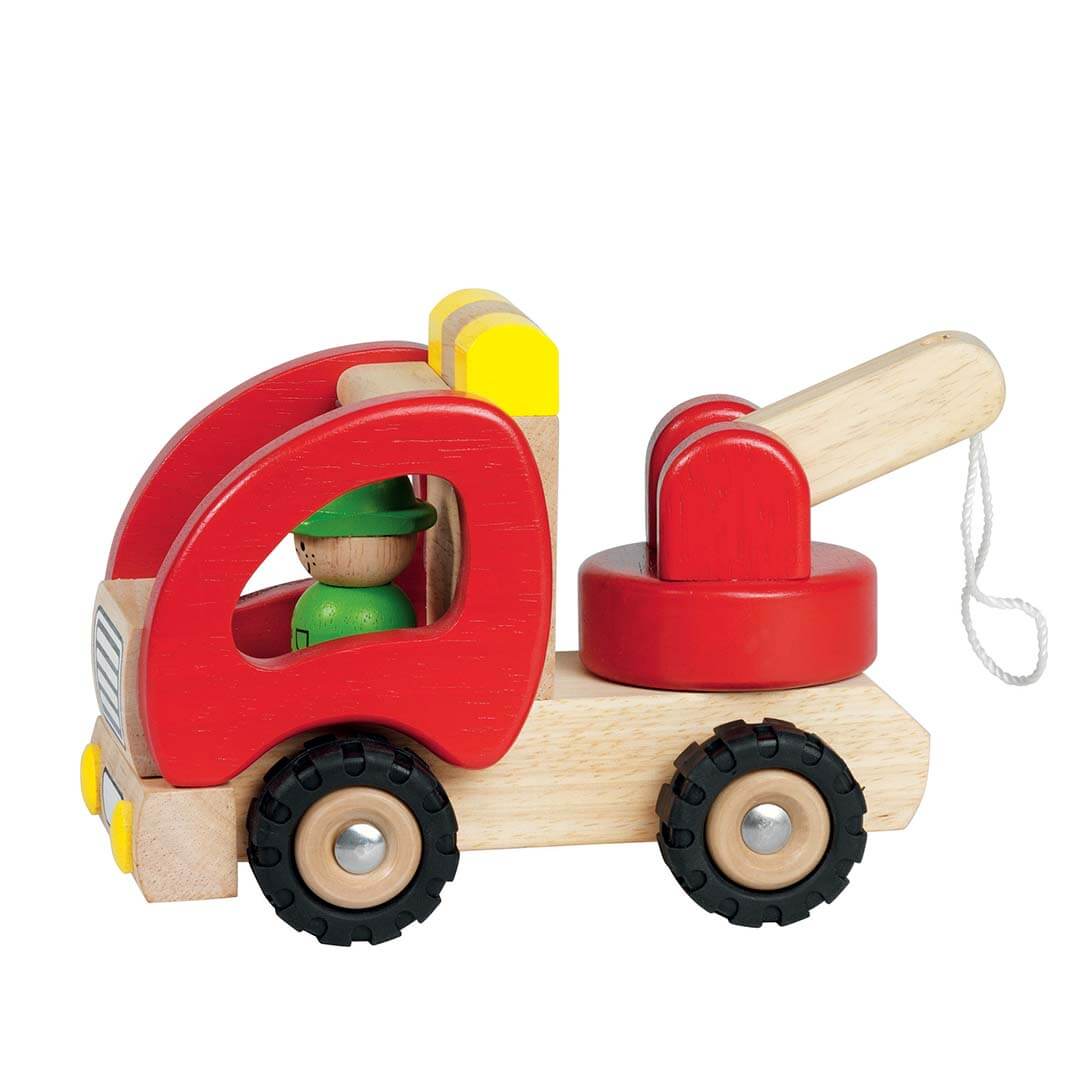 A wooden toy tow truck with a red cab, natural wood chassis and arm, black wheels, and a small green figure in the driver's seat, shown on a plain white background.