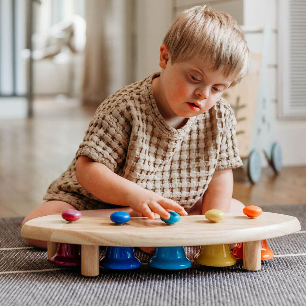 A toddler sitting in front of the pentatoic pat bell station, tapping on one of the bells.