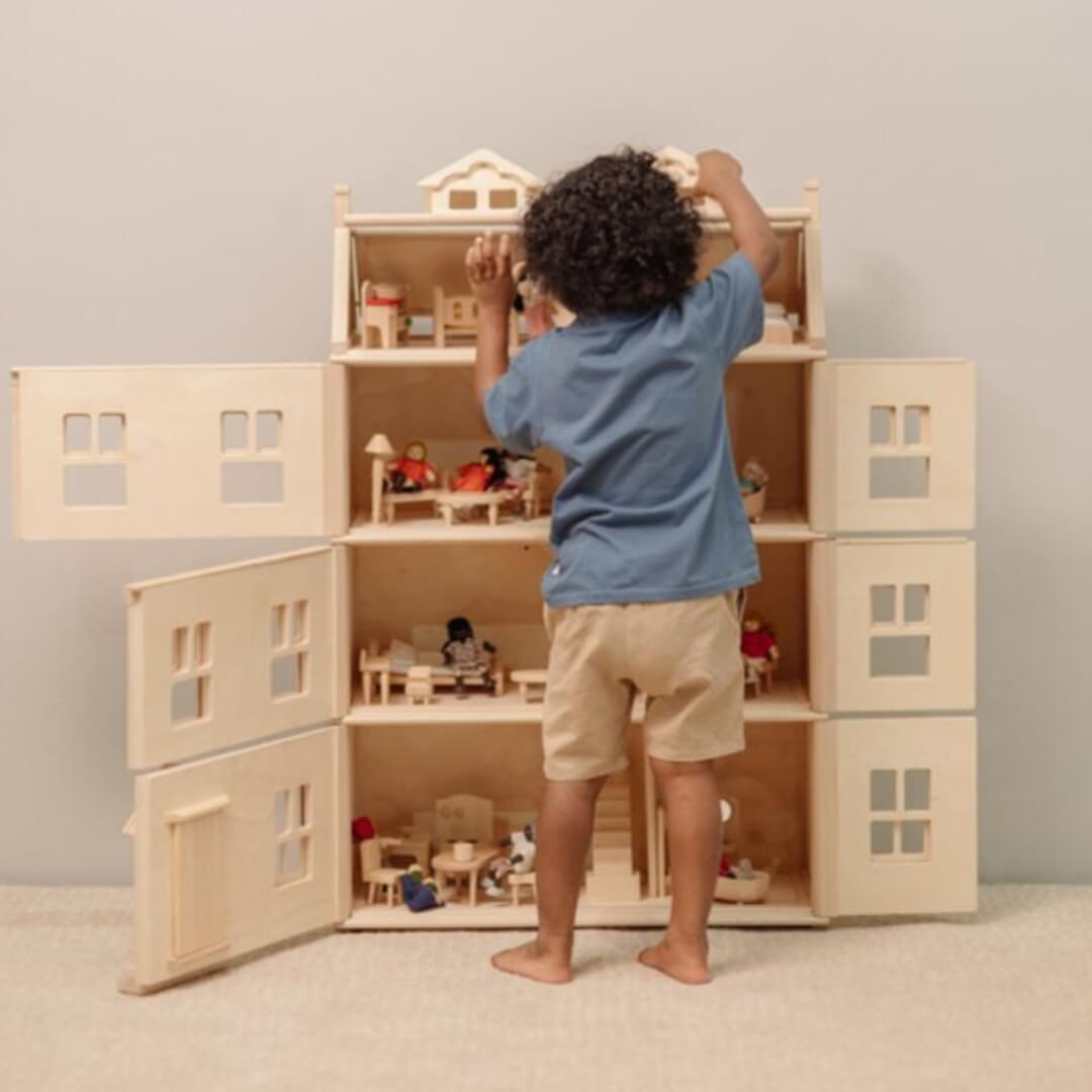 Child standing in fron of the Four-story PlanToys Grand Victorian Wooden Dollhouse with with all of the various levels open and furnished. Bella Luna Toys