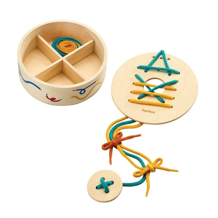 PlanToys Montessori Lacing Set with round wooden container, lacing boards, and colorful strings threaded in patterns.