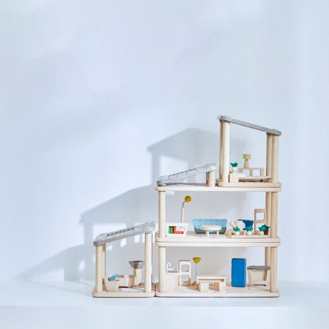 PlanToys PlanSpace modular dollhouse setup in a traditional way displayed on a white background, featuring multiple wooden rooms with furniture, potted plants, and a modern open design.