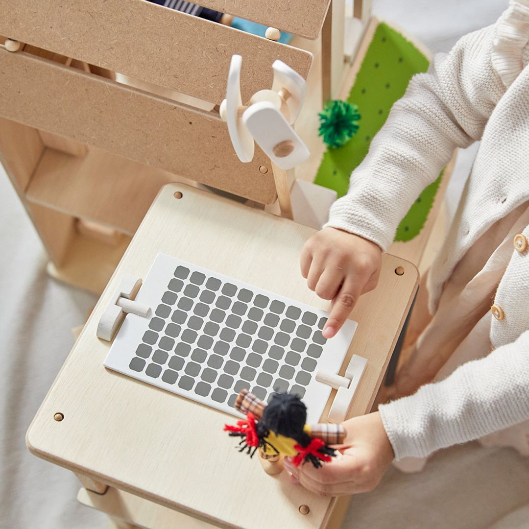 A child holding a wooden dollhouse figure on the roof of the PlanToys Green Dollhouse featuring a wind turbine and solar panel.