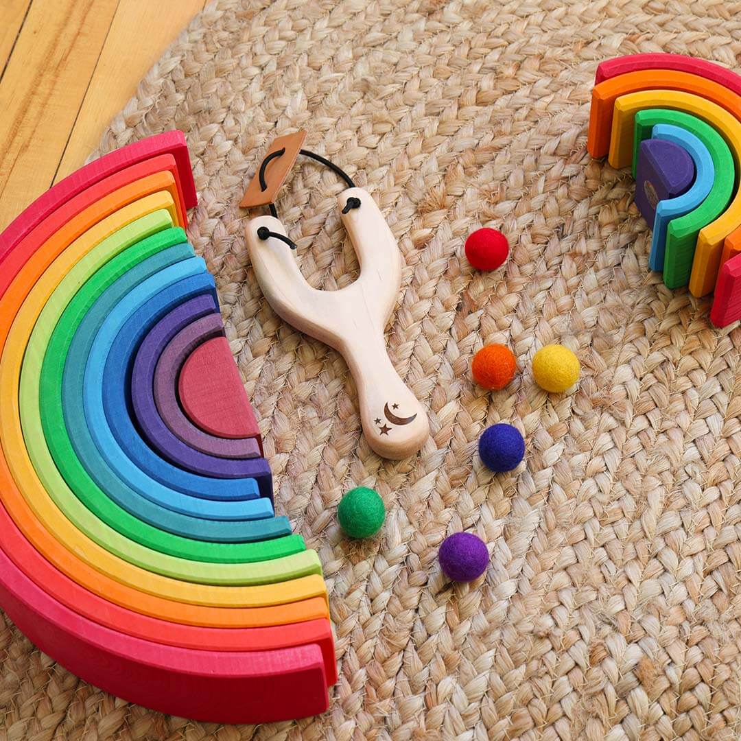 Colorful wooden toys including a rainbow, slingshot, and colorful balls on a woven surface.