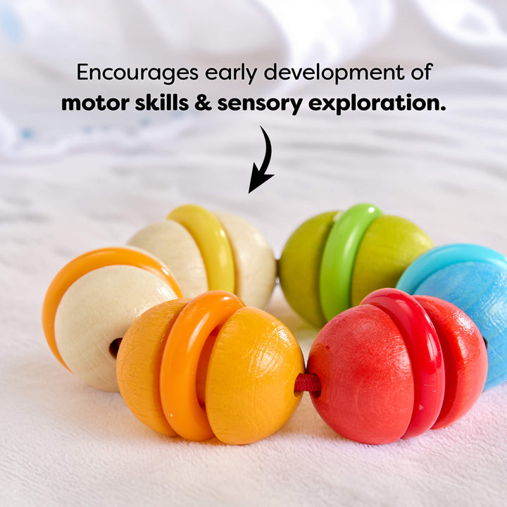 Colorful wooden baby rattle on a white blanket with text about developmental benefits.