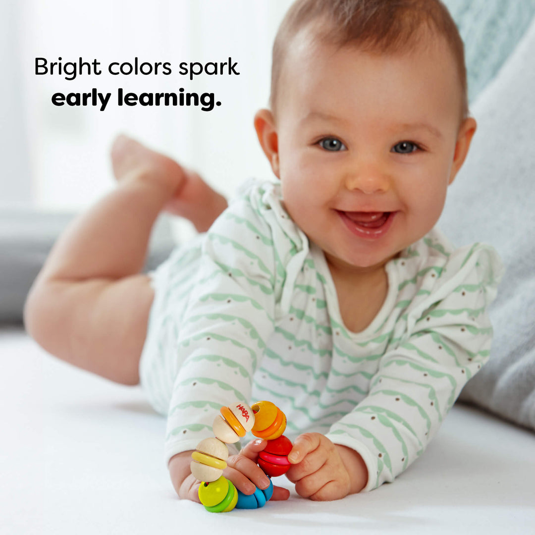 Baby playing with a colorful toy on a light surface, with text 'Bright colors spark early learning.'