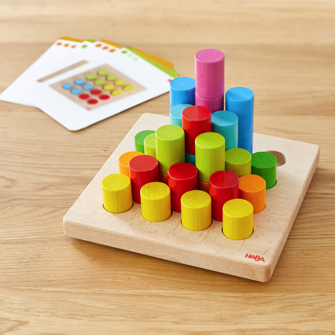 Colorful cylinders on a wooden board with pattern cards in the background.